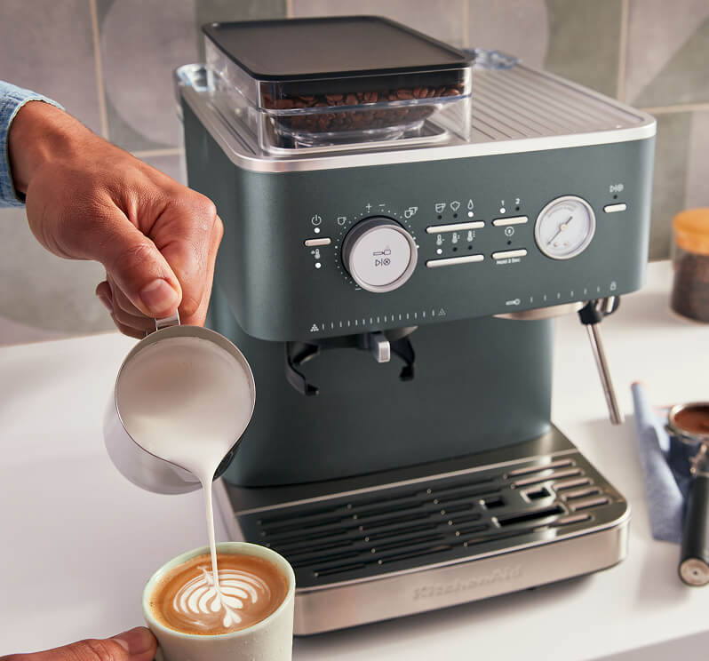 A person pouring milk into a mug to make latte art.